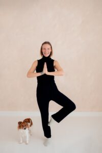 Die Stress- und Lifecoachin macht eine Yogaübung. Neben ihr steht ihr kleiner Hund.