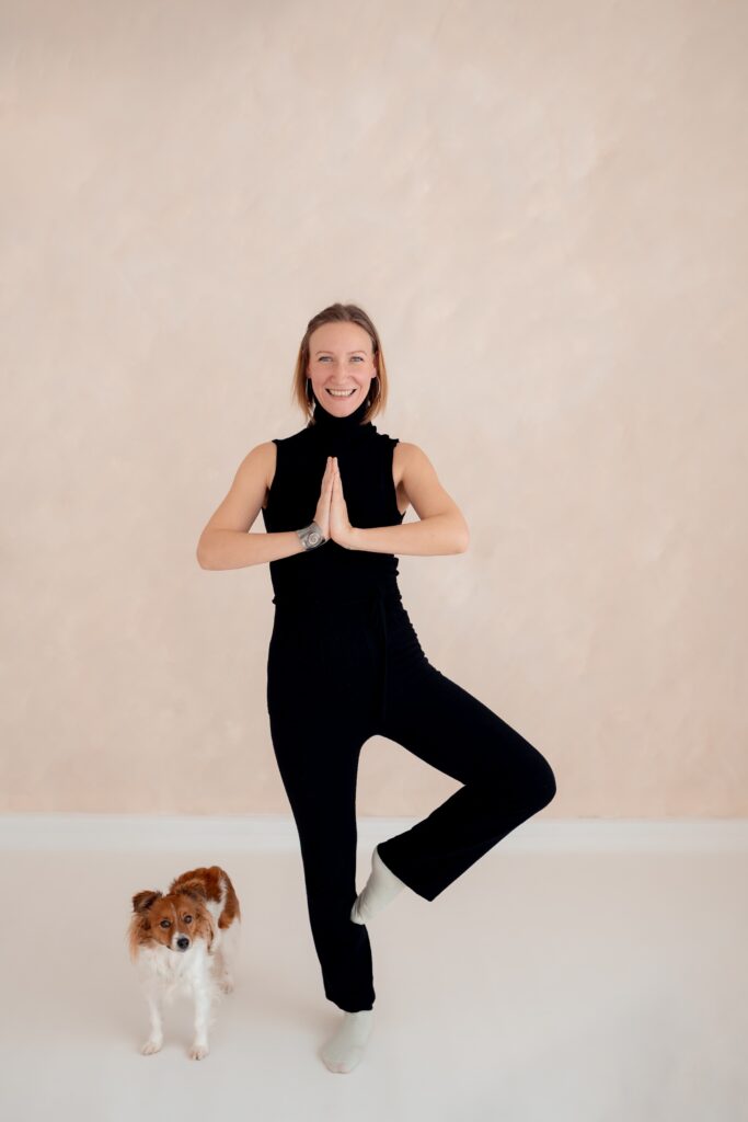 Die Stress- und Lifecoachin macht eine Yogaübung. Neben ihr steht ihr kleiner Hund.