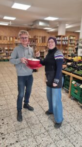 Die Inhaber halten im Lebensmittelgeschäft lächelnd eine übergroße Tasse.