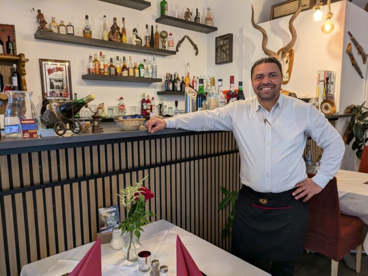 Der Inhaber lehnt lächelnd an der Theke seines Restaurants.