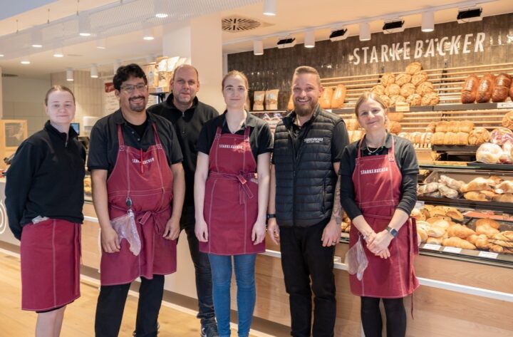 Gruppenfoto: Das Team des Bäckers steht vor der Ladentheke und lächelt herzlich in die Kamera.