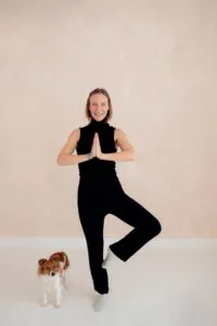 Die Stress- und Lifecoachin macht eine Yogaübung. Neben ihr steht ihr kleiner Hund.