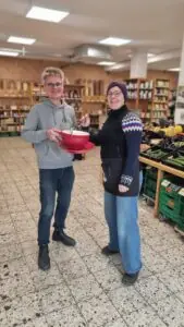 Die Inhaber halten im Lebensmittelgeschäft lächelnd eine übergroße Tasse.