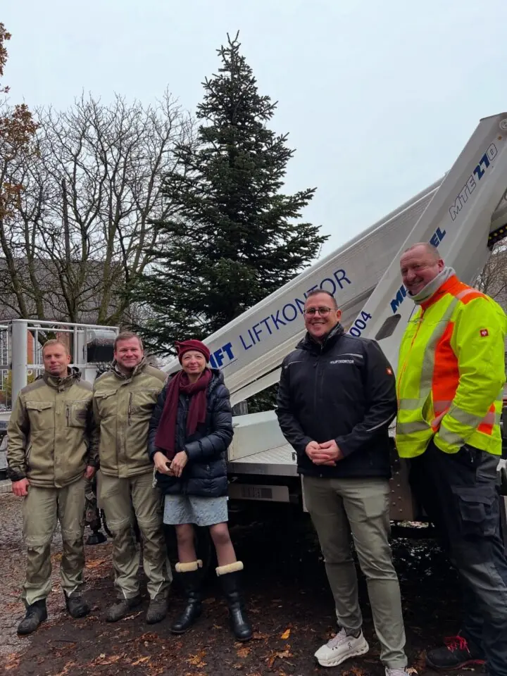 Auf dem Foto sind fünf lächelnde Personen vor einer Hebebühne und einem Tannenbaum zu sehen.