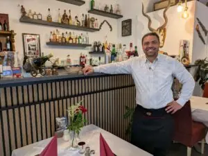 Der Inhaber lehnt lächelnd an der Theke seines Restaurants.