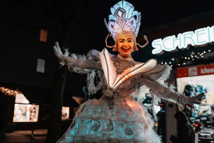 Freudige Darstellerin der Leuchtfigur von Stelzen-Art in der nächtlichen Hemmstraße beim Weihnachtsbummel