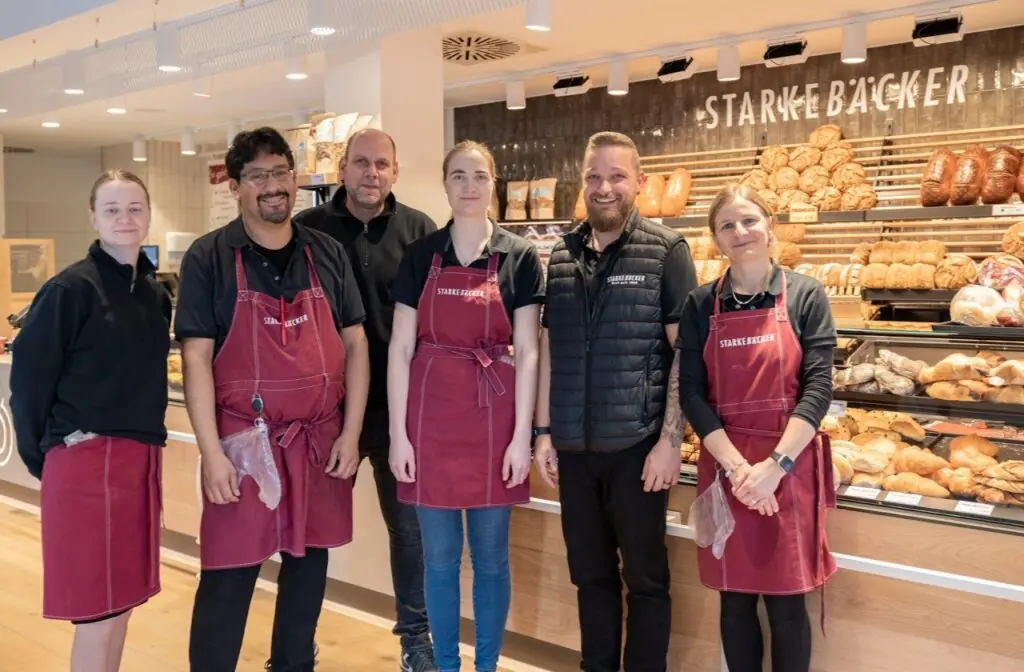 Gruppenfoto: Das Team des Bäckers steht vor der Ladentheke und lächelt herzlich in die Kamera.