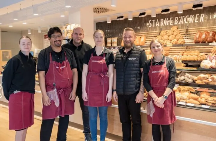 Gruppenfoto: Das Team des Bäckers steht vor der Ladentheke und lächelt herzlich in die Kamera.